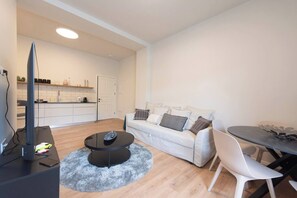 A modern living room with a sofa, a coffee table, a TV, and a dining area with a table and chairs. - Haifa German Colony 2BR Apt, Sleeps 5 (Haifa)