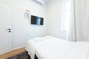 Une chambre d’hôtel avec un lit, un téléviseur à écran plat fixé au mur, une porte et une fenêtre avec des rideaux.