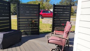 Eine Terrasse mit überdachter Sitzgelegenheit, ein roter SUV im Hintergrund und ein schwarzer Zaun mit gelben Linien.