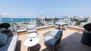 Una terraza en la azotea con mobiliario moderno, vistas al mar y edificios urbanos al fondo.