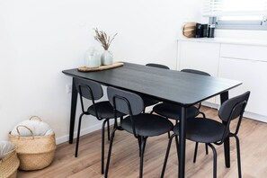 A modern dining area with a dark wooden table and black chairs, a white cabinet, and a basket with white cushions. - Port city - Seaview Penthouse w/ Jaccuzzi + mamad (Haifa)