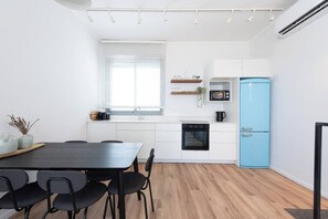 A modern kitchen with white cabinetry, a blue refrigerator, and a dining area with a black table and chairs. - Port city - Seaview Penthouse w/ Jaccuzzi + mamad (Haifa)