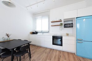 Eine moderne Küche mit weißen Schränken, einem schwarzen Geschirrspüler, einem blauen Kühlschrank und einem Essbereich mit Tisch und Stühlen.
