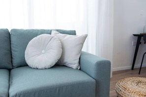 A light blue sofa with two white pillows, a woven basket, and a small table with a lamp. - Port city - Seaview Penthouse w/ Jaccuzzi + mamad (Haifa)