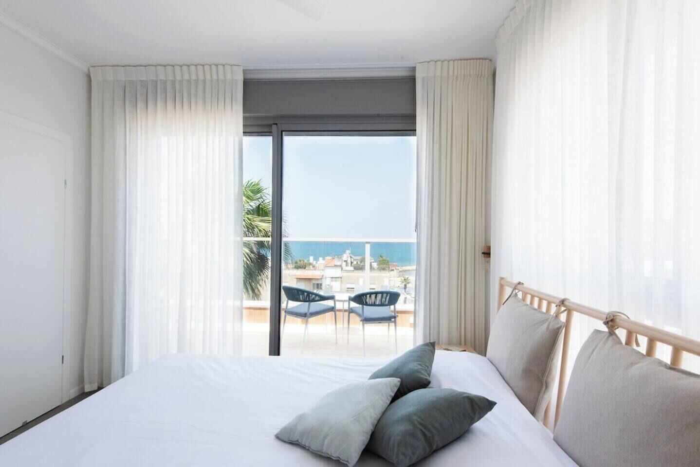 A hotel room with a bed, two pillows, a balcony with a table and chairs, and a view of the sea.