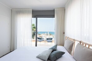 Ein Hotelzimmer mit Bett, zwei Kissen, einem Balkon mit Tisch und Stühlen sowie Meerblick.
