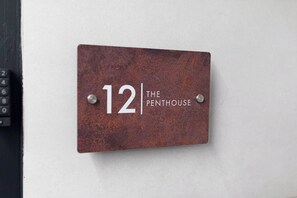 Eine Metallplatte mit der Nummer 12 und dem Schriftzug 'THE PENTHOUSE', an einer Wand angebracht.