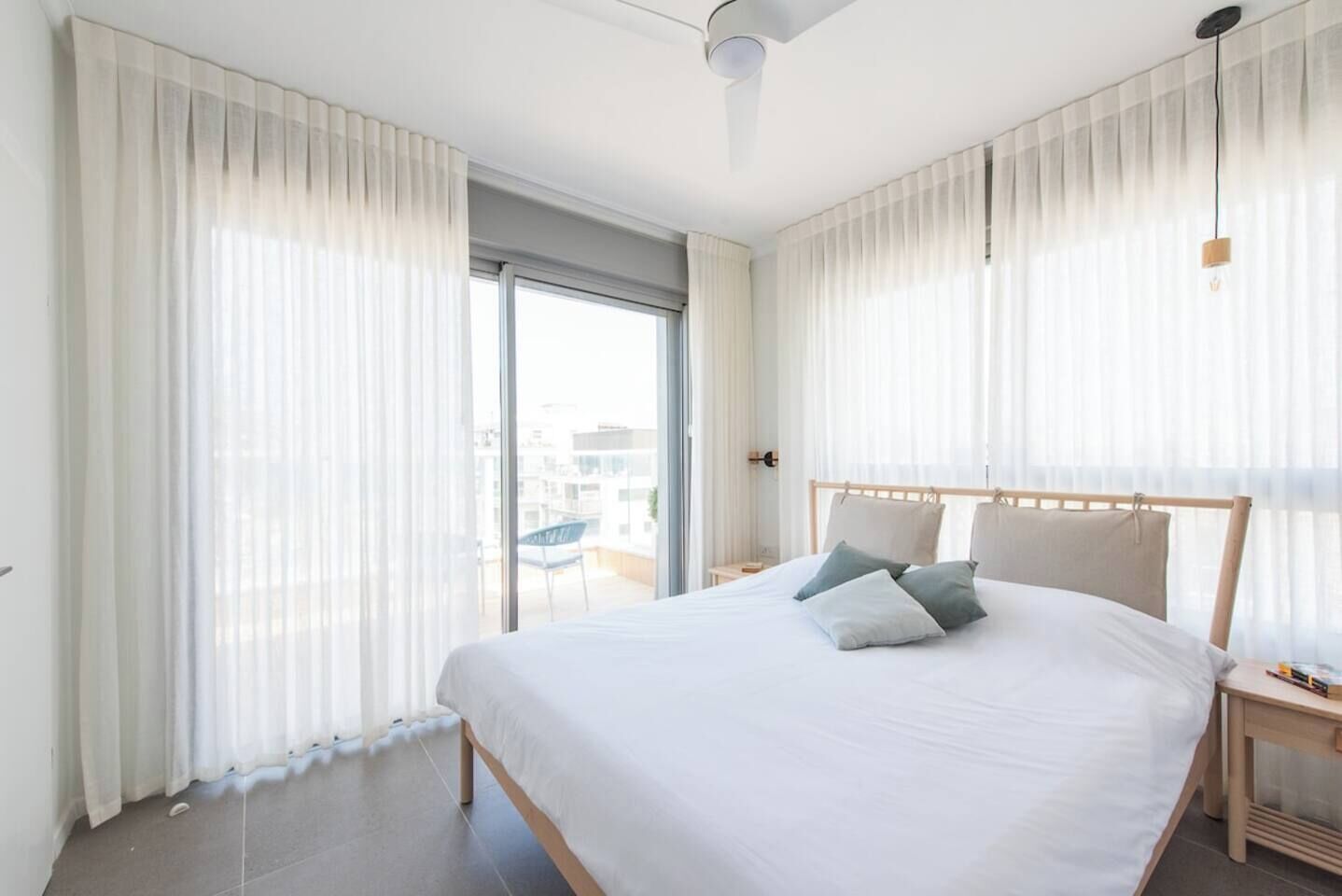 Habitació d'hotel moderna amb un llit gran, un panell de capçalera de fusta i cortines de tul.