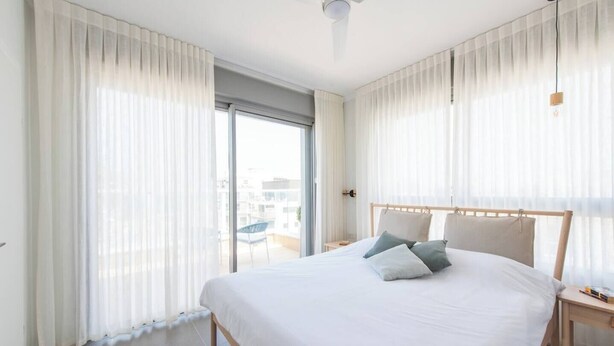 Ein modernes Hotelzimmer mit einem großen Bett, einem Holz-Kopfteil und transparenten Vorhängen.