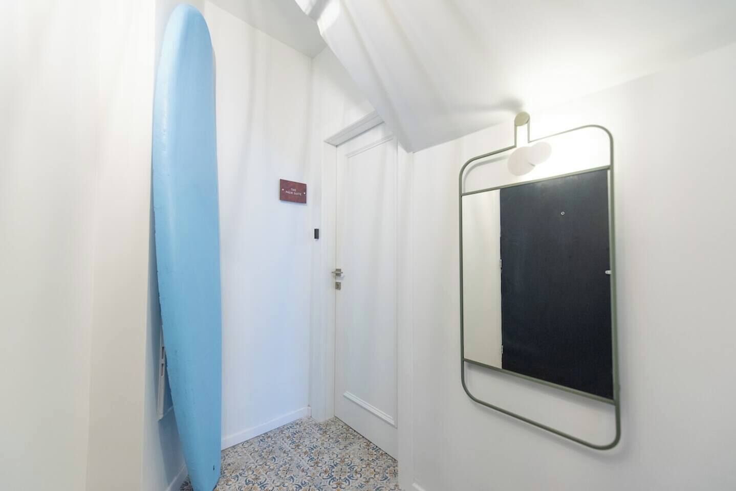En hall med en blå surfbräda lutad mot väggen, en dörr med en skylt och en spegel på väggen.