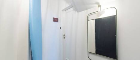 En hall med en blå surfbräda lutad mot väggen, en dörr med en skylt och en spegel på väggen.