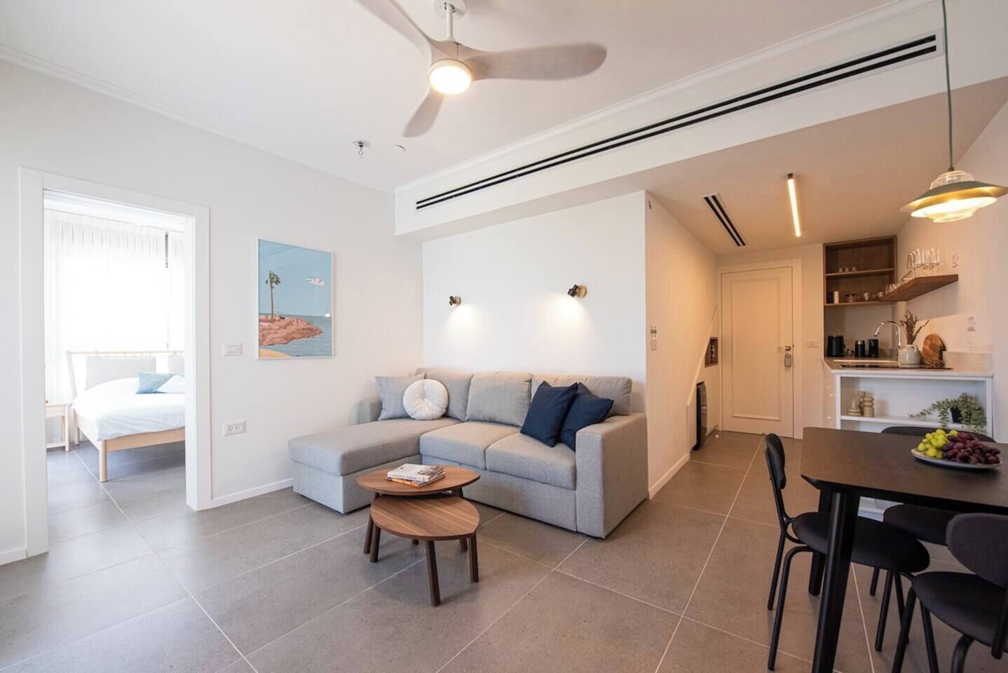 Uma sala de estar moderna com um sofá cinzento, uma mesa de centro e um espaço de jantar com uma mesa posta para dois.