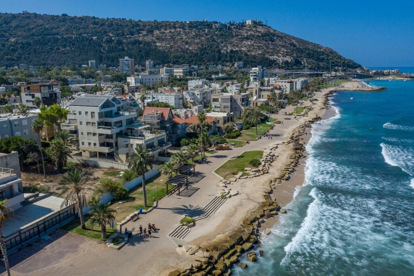 A coastal town with a beachfront, residential buildings, and a hilly backdrop.