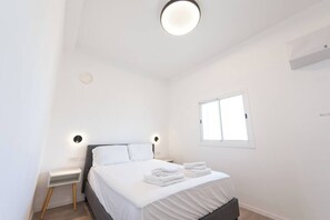 Ein schlicht eingerichtetes Schlafzimmer mit Bett, Nachttischen und einem Fenster.