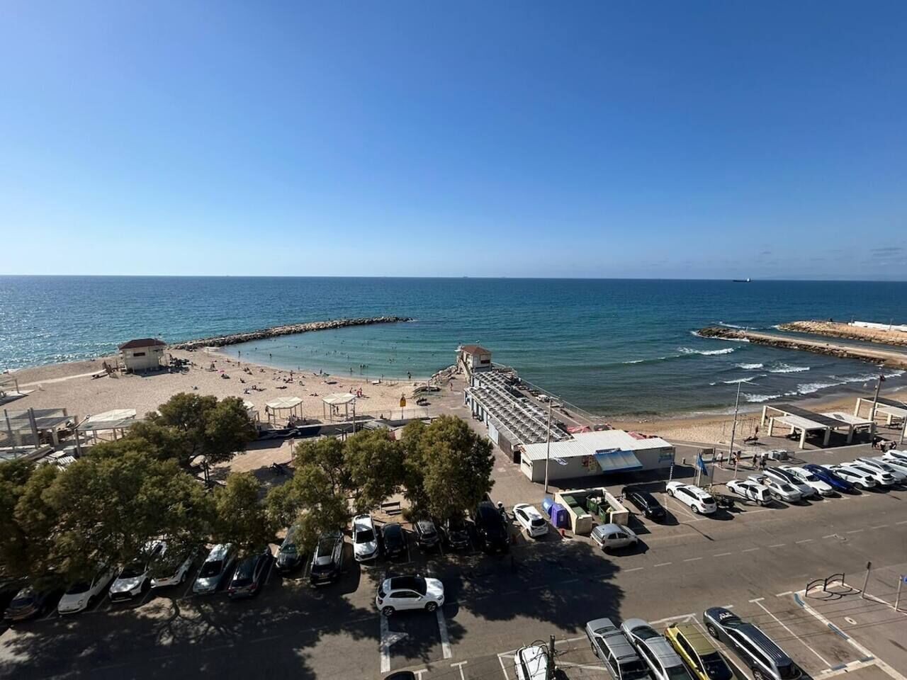 Eine Küstenlandschaft mit Strand, Parkplatz und einem Gebäude mit Satteldach.
