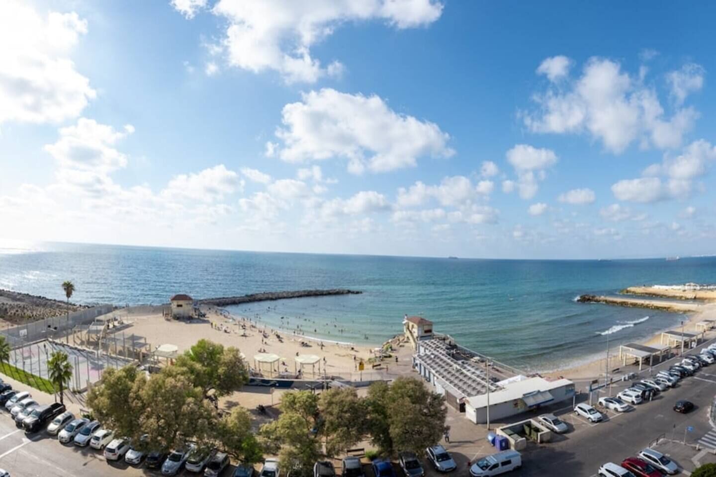 Zona costera con playa, muelle y estacionamiento con automóviles.