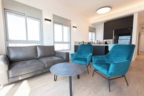Ein modernes Wohnzimmer mit einem grauen Sofa, zwei türkisfarbenen Sessel und einem kleinen runden Tisch.
