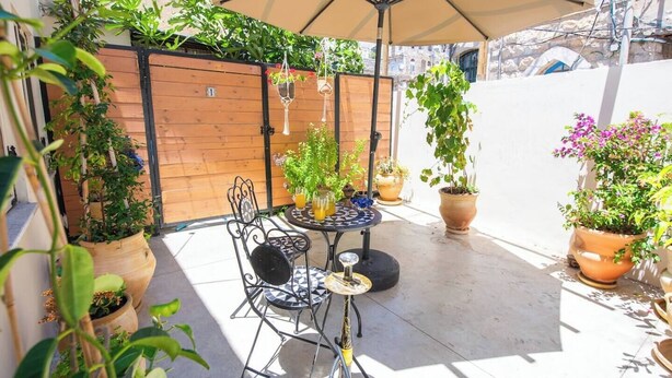 Un patio exterior con una mesa y sillas, rodeado de plantas en macetas y una valla de madera.