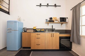 A compact kitchen with a blue refrigerator, wooden cabinets, a microwave, and a coffee maker. - Port city haifa - Downtown Urban Oasis w Yard (Haifa)