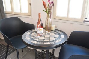 Een ronde tafel met een mozaïek blad, twee zwarte stoelen, een wijnfles, een kaars en een vaas met bloemen.