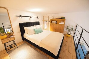 A bedroom with a bed, bedside table, mirror, wardrobe, and a potted plant. - Port city haifa - Downtown Urban Oasis w Yard (Haifa)