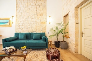 Ein Wohnzimmer mit einem türkisfarbenen Sofa, einem Glastisch, einem gemusterten Teppich, einer Topfpflanze und einer Steinwand.