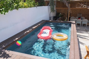 Ein kleiner Pool mit Holzterrasse, umgeben von einer weißen Mauer und einem Bambuszaun.