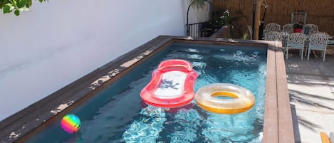 A swimming pool with a wooden deck, a lounge area with chairs, and a thatched roof structure.