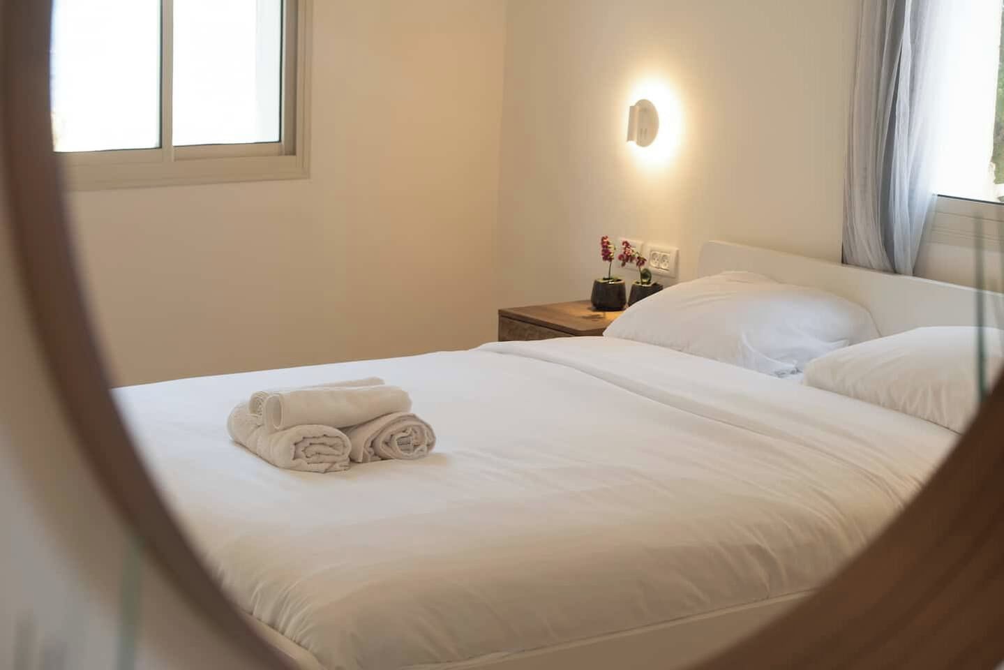 Habitació d'hotel amb un llit ben fet, una taula de nit amb una làmpada i una finestra amb cortines.