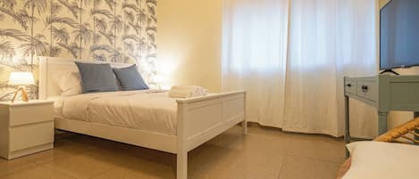 A bedroom with a bed, bedside tables, a television, and a window with curtains.