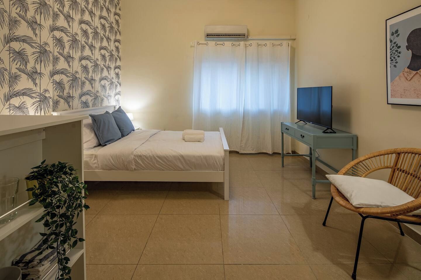 Ein Schlafzimmer mit Bett, Fernseher, Sessel und Zimmerpflanze.