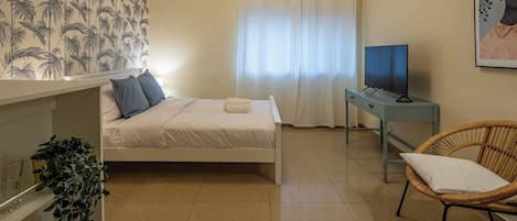 Un dormitorio con una cama, televisor, sillón y una planta.