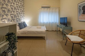 A bedroom with a bed, a TV, a chair, and a plant. - Port City Haifa - Cozy Downtown studio (Haifa)