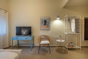Een hotelkamer met een bed, een bureau met een televisie, een rieten stoel, een klein tafeltje met een vaas en een inbouwkast.