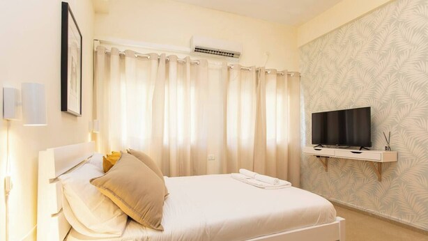 Quarto de hotel com cama, cortinas, televisão e uma estante fixada na parede.