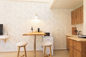 Eine kleine Küche mit einem Holztisch, zwei Barhocker, einer Mikrowelle und einem kleinen Kühlschrank.