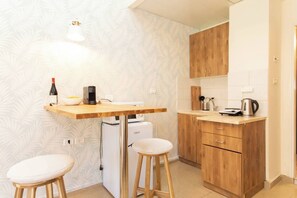 Une cuisine compacte avec un plan de travail en bois, un petit réfrigérateur et un four à micro-ondes. On y trouve deux tabourets et un seul luminaire au-dessus du plan de travail.