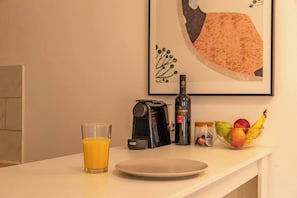 A kitchen counter with a coffee maker, a bottle of wine, a glass of orange juice, a bowl of fruit, and a framed picture on the wall. - Downtown Haifa Studio 212, Near Port, AC & WiFi (Haifa)