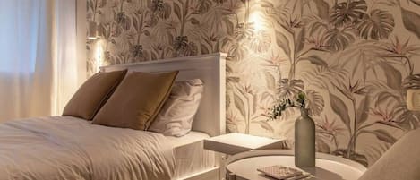 A bedroom with a bed, bedside table, and a round table with a vase.