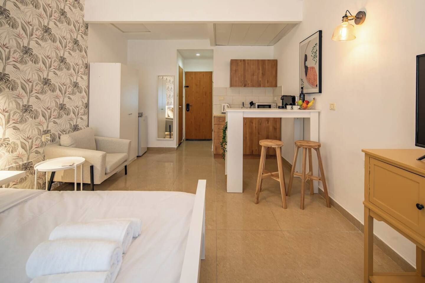 Habitación de hotel con cama, una mesita, sofá, kitchenette y un baño al fondo.