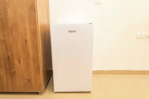 Ein weißer Kühlschrank mit dem Schriftzug 'Fujicorm', neben einem Holzschrank in einem Raum mit Fliesenboden.