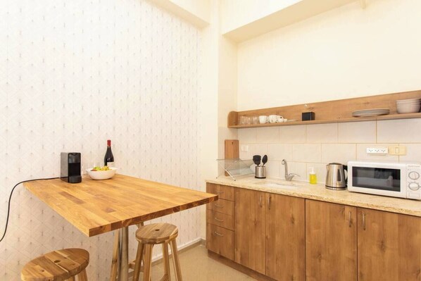 A compact kitchen with a wooden table, stools, a wine bottle, a coffee maker, a kettle, and a microwave. - Port city haifa - Downtown 213 (Haifa)