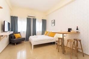 Ein kleines Hotelzimmer mit einem Bett, einem Schreibtisch, einem Stuhl, einem Fernseher und einem Fenster mit Vorhängen.