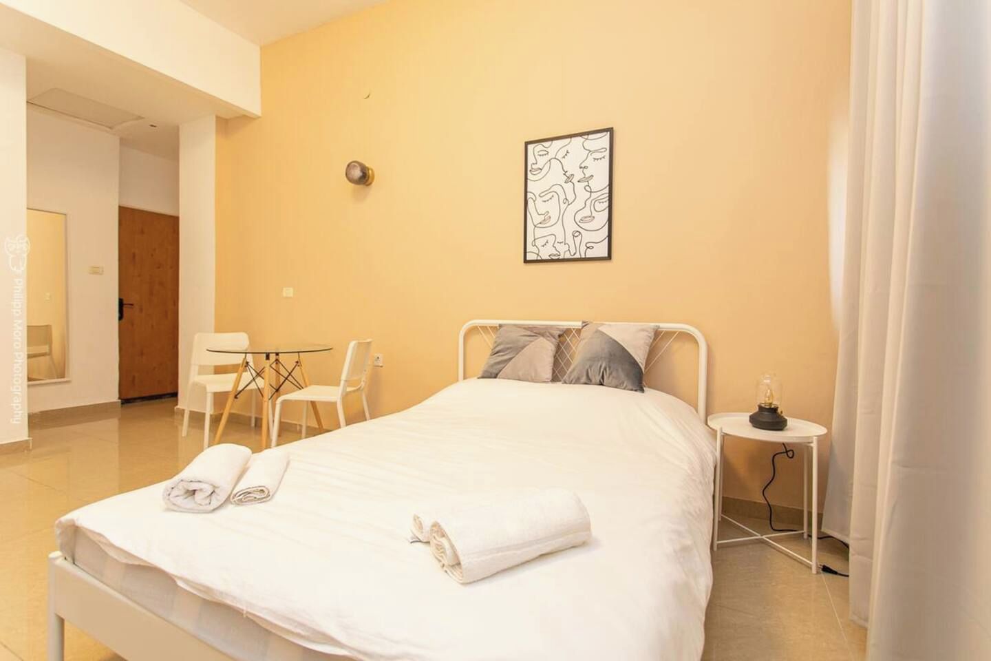 A hotel room with a bed, a bedside table with a lamp, a chair, and a small table with chairs.