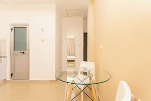 Ein Hotelzimmer mit Glastisch, weißen Stühlen, einer Tür mit Milchglasfenster und einem hellen Boden.
