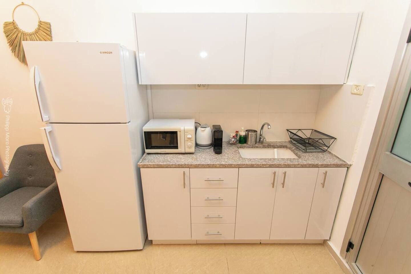 Una cocina compacta equipada con refrigerador, microondas, cafetera y lavamanos.