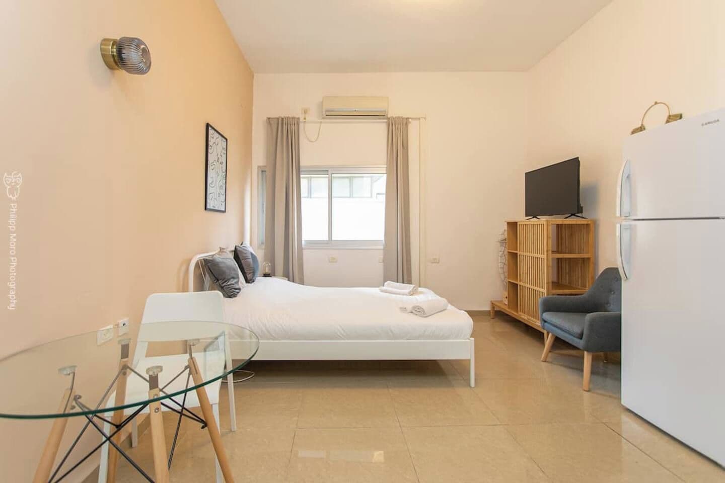 A bedroom with a bed, a television, a refrigerator, a chair, and a wooden cabinet.