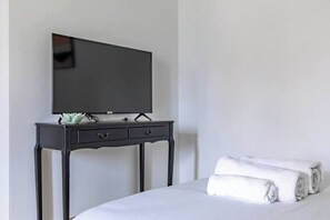 Une chambre d’hôtel avec un lit, un téléviseur à écran plat posé sur un meuble en bois foncé, et une serviette enroulée sur le lit.