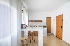 A modern kitchen with white cabinetry, a wooden door, and a small dining area with stools. - Downtown Haifa Studio 215, Near Port, AC & WiFi (Haifa)