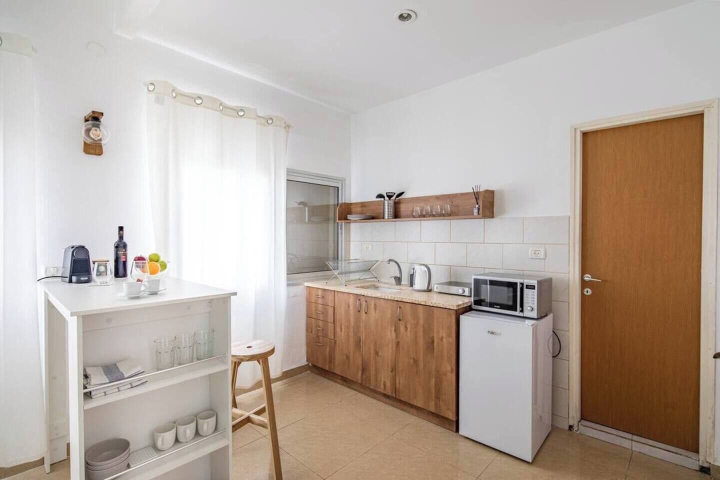 Une cuisine compacte avec des meubles blancs, un four à micro-ondes, une bouilloire et un petit réfrigérateur.